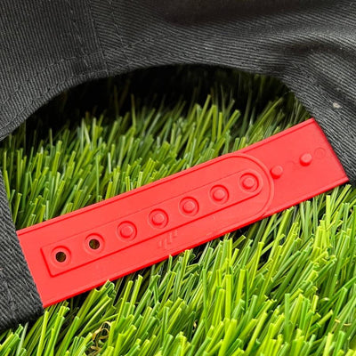A black dzdiscs yupoong flat bill snapback cap with a bright red plastic snap closure over green artificial grass.