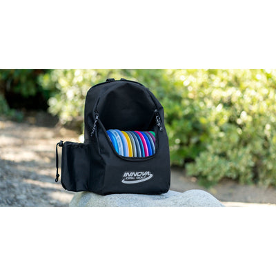 Black innova discover disc golf bag with a vibrantly colored assortment of discs, sitting on a rock.