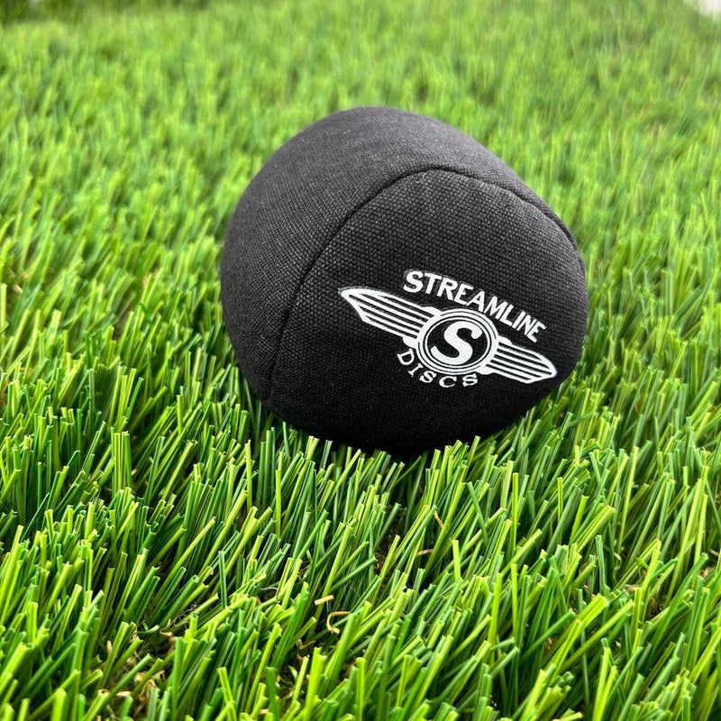 Black streamline osmosis sport ball bag with white logo, resting on bright green artificial turf.