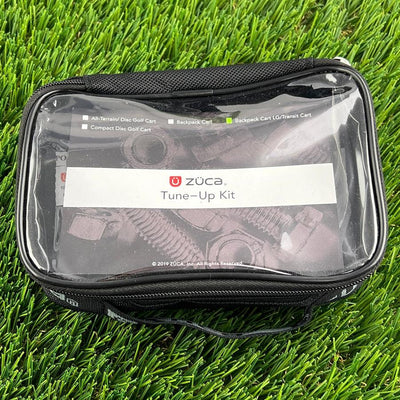 Black zuca tune-up kit in a clear zipper pouch showing bolts and nuts, resting on green artificial turf.