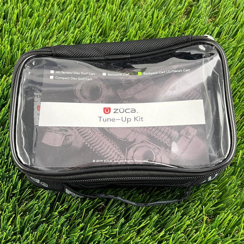 Black zuca tune-up kit in a clear zipper pouch showing bolts and nuts, resting on green artificial turf.