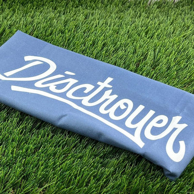 A blue disctroyer nightjar microfiber towel with white lettering lies on vibrant green artificial grass.