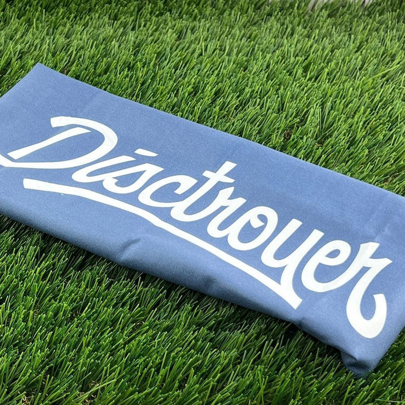 A blue disctroyer nightjar microfiber towel with white lettering lies on vibrant green artificial grass.
