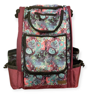 Carbella Designs disc golf backpack in mauve with an abstract watercolor print and black zippers on the pockets.