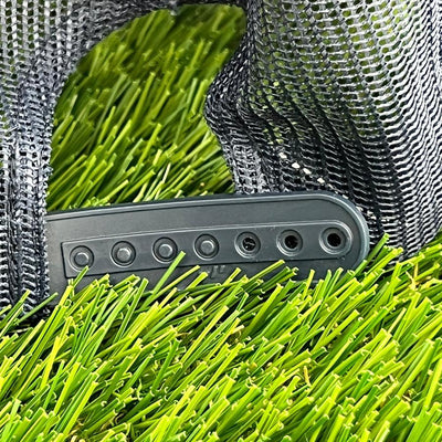 Close-up of a black mesh trucker cap's adjustable snapback clasp resting on bright green artificial turf.