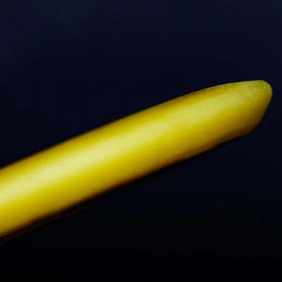 A close-up of a yellow rod-shaped dg max wax mini grip wax with a rounded edge, angled against a dark background.