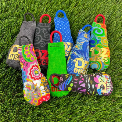 Colorful "moon tear" grip sacks by dzdiscs, featuring various patterns, loops, and the brand logo, scattered on green turf.
