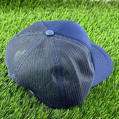 Dark blue yupoong foam trucker snapback cap with mesh back and matching button, resting on green artificial turf.