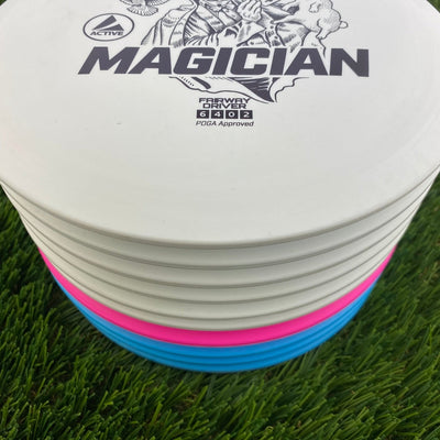 Stack of white Discmania Active Base Level Magician fairway drivers with faint pink and blue discs visible toward the bottom.