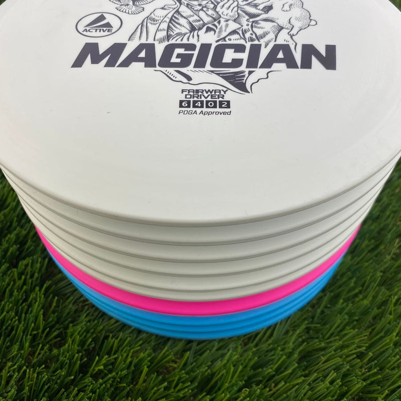 Stack of white Discmania Active Base Level Magician fairway drivers with faint pink and blue discs visible toward the bottom.