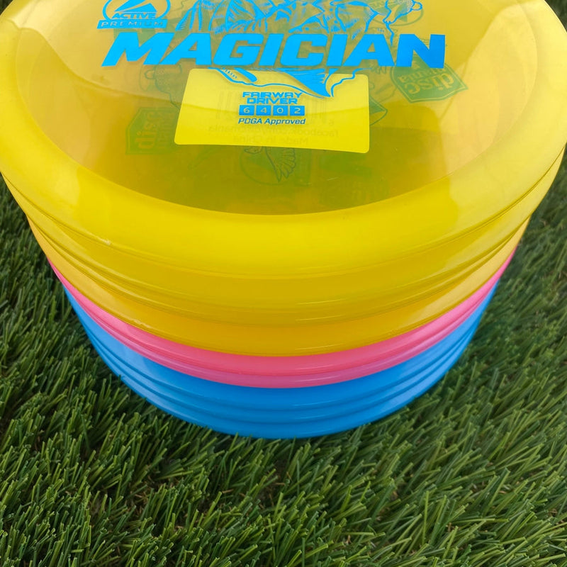 Stack of yellow, pink, and blue Discmania Active Premium Magician disc golf fairway drivers with flight numbers 6 4 0 2.