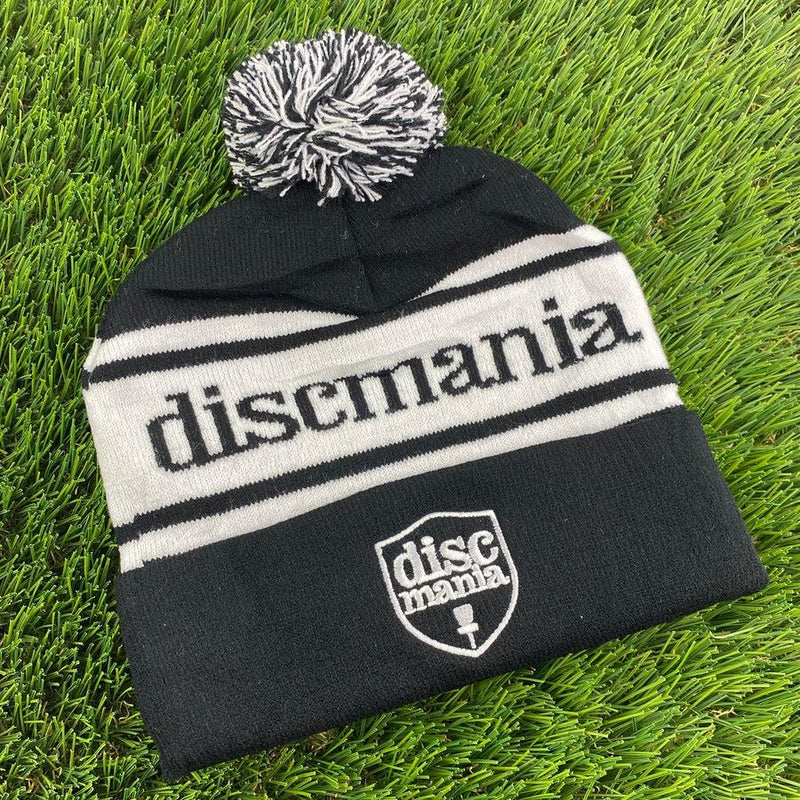 Black Discmania woven pom beanie with a black and gray pom, a white Discmania logo, and white stripes.