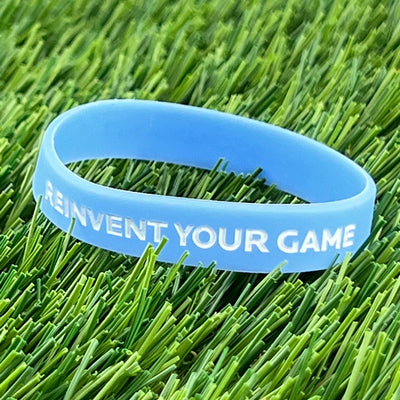 Light blue Discmania Reinvent Your Game silicone wristband with white embossed text.