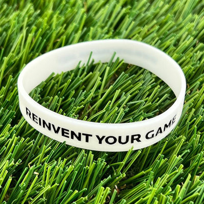 Discmania “REINVENT YOUR GAME” white silicone wristband with bold black lettering on a textured surface.