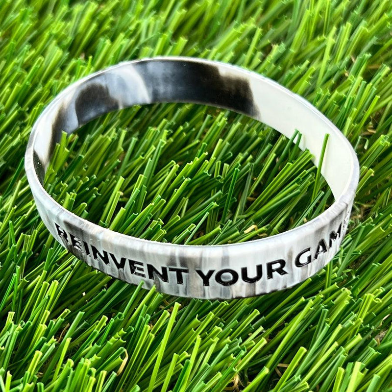 Discmania Reinvent Your Game wristband featuring a marbled grey and white silicone band with black embossed text.
