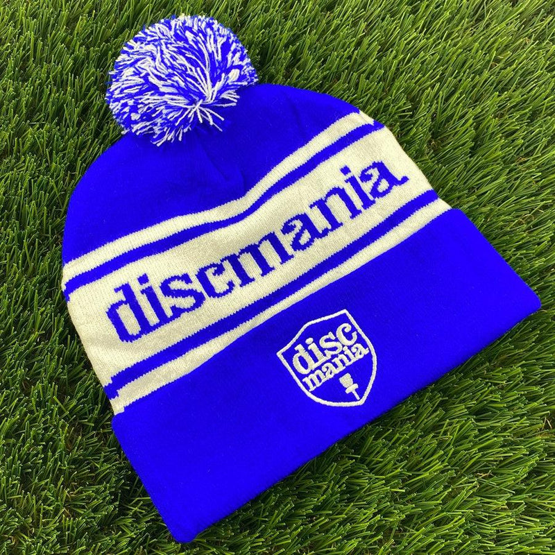 Royal blue and white Discmania pom beanie with "discmania" knitted across the crown and a logo on the cuff.