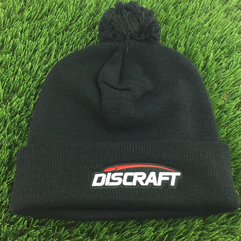 Black knit Discraft embroidered logo cuff pom beanie with a red stripe above white lettering.