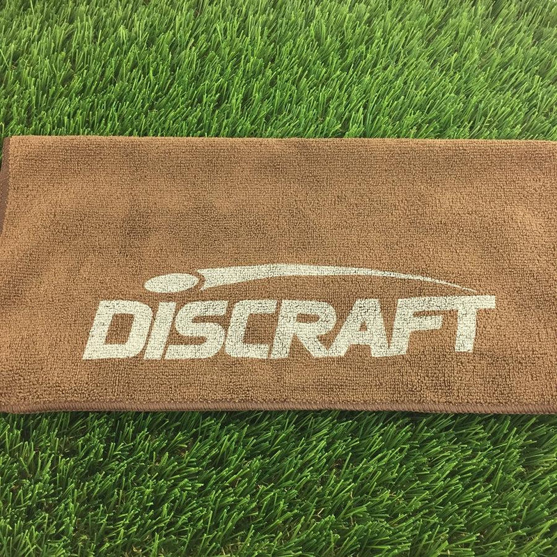 Brown microfiber golf towel with a white printed Discraft logo and a dark brown stitched border.