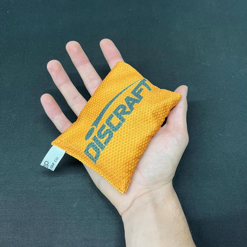Orange Discraft Silky Feel Waffle Sportsack with black Discraft logo held in an open hand.