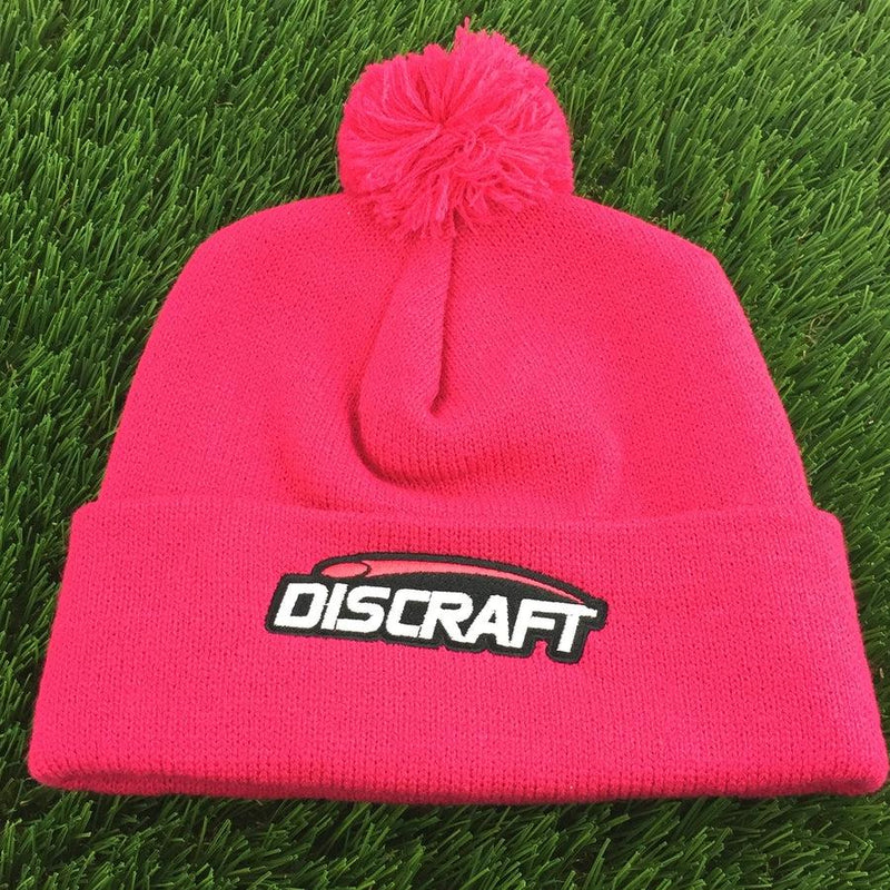 Bright pink Discraft knit beanie featuring an embroidered logo on the cuff and a matching pom on top.