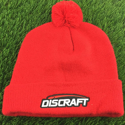 Red knit Discraft embroidered logo cuff pom beanie with a fluffy pompom on top and a white and black logo.