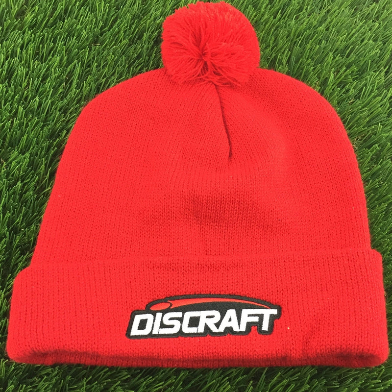 Red knit Discraft embroidered logo cuff pom beanie with a fluffy pompom on top and a white and black logo.
