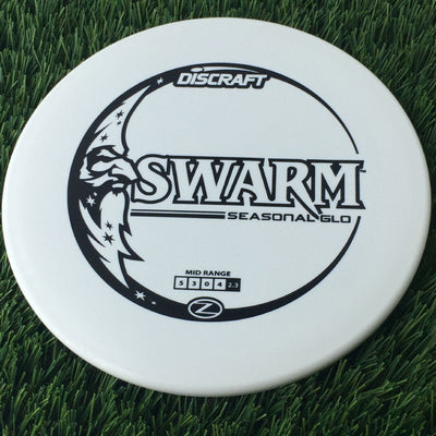 Solid white Discraft Seasonal Glo Elite Z Swarm disc golf mid-range disc with a black moon and stars stamp.