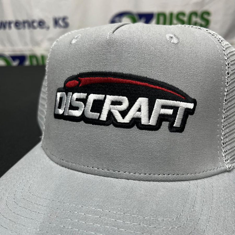 Light gray trucker hat with a white Discraft embroidered logo outlined in black, featuring a red and black stylized swoosh.