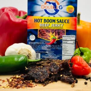 DoubleG Hot Boom Sauce Craft Beef Jerky bag with red bell peppers, garlic, and chili flakes on a wooden surface.