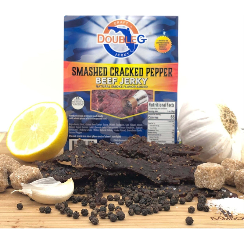 DoubleG Smashed Cracked Pepper Beef Jerky package behind dark jerky, whole peppercorns, garlic, and cubed brown sugar.