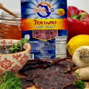 A blue and yellow Double G Teriyaki Beef Jerky package stands upright next to a pile of dark brown jerky pieces.