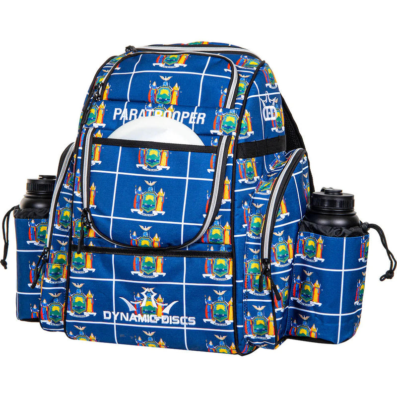 Blue Dynamic Discs Paratrooper backpack with a white grid pattern, multiple zippered pockets, and two black water bottles.
