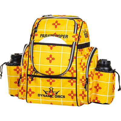 Yellow Dynamic Discs Paratrooper backpack disc golf bag with red Zia symbols, black trim, and bottle holders.