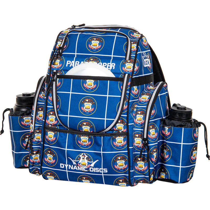 Blue Dynamic Discs Paratrooper backpack with a white grid pattern, Utah state emblems, and two water bottles.