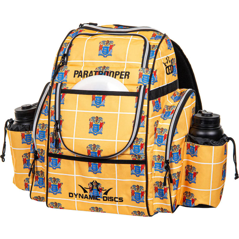 Yellow Dynamic Discs Paratrooper disc golf bag with a New Jersey state seal pattern and two black water bottles.