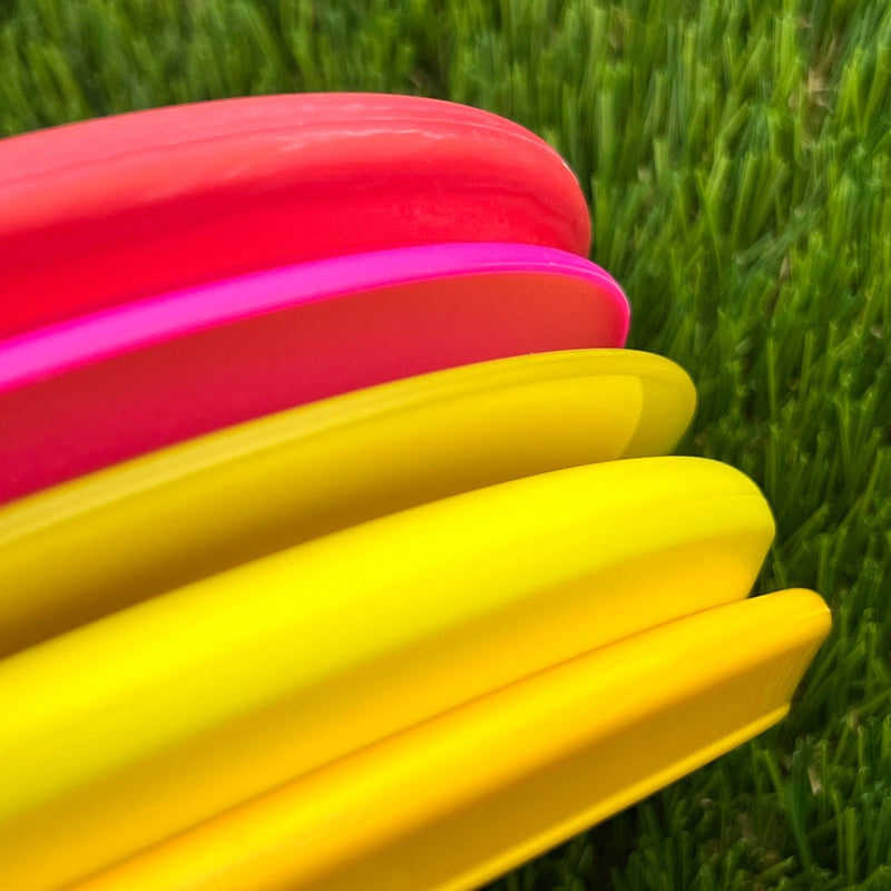 Four vibrant disc golf discs are stacked together, featuring one bright fuchsia and three sunshine yellow discs.