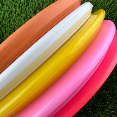 A fanned assortment of five disc golf discs in orange, white, yellow, light pink, and red colors.