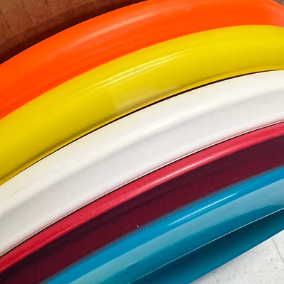A vibrant stack of disc golf discs in orange, yellow, white, red, and blue with varied rims.
