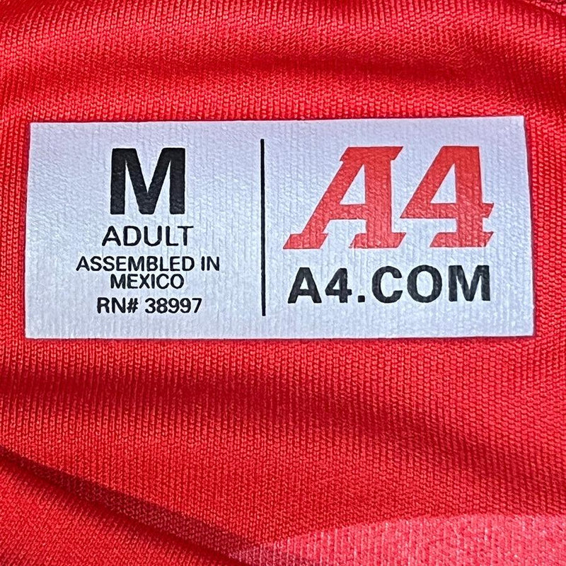 White A4 brand label on a red dry-fit performance shirt with M adult sizing and "Assembled in Mexico" text.