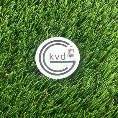 Round white KVD Disc Golf disc golf sticker with a black logo featuring a basket and letters.