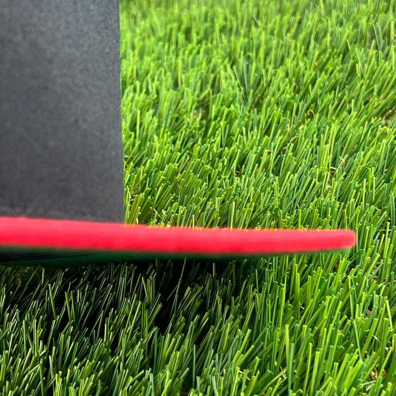 Edge of a black dzdiscs yupoong flat bill snapback cap with a red brim resting on green artificial turf.