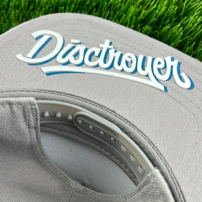 Gray flat bill snapback hat with "disctroyer" in raised white and blue lettering, on green grass.