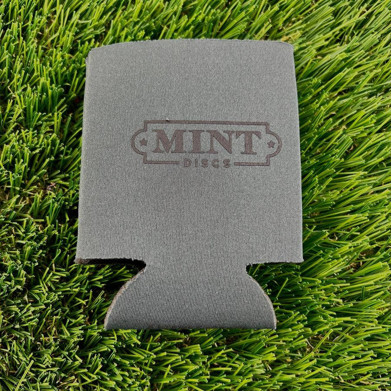 Gray neoprene beverage koozie featuring the "mint discs" logo, resting on vibrant green artificial turf.