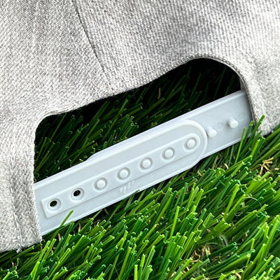 Gray premium yupoong curved bill snapback cap with a light gray snapback closure, resting on green artificial turf.