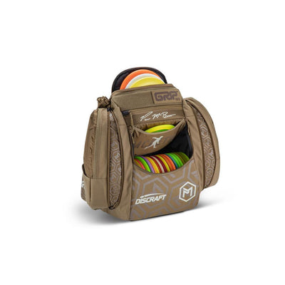 Brown GRIP EQ AX5 Paul McBeth disc golf bag with colorful Discraft discs and silver geometric patterns.