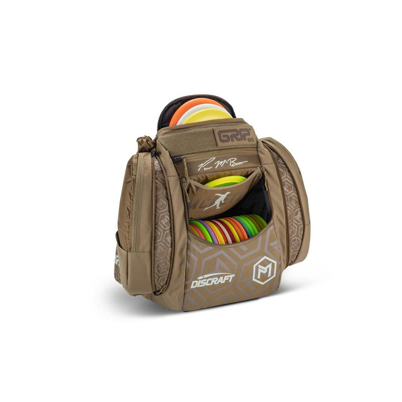Brown GRIP EQ AX5 Paul McBeth disc golf bag with colorful Discraft discs and silver geometric patterns.
