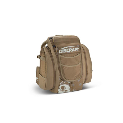 Tan Discraft Buzzz BX3 disc golf backpack with multiple zippered pockets and a white skull logo.