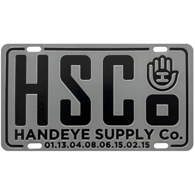Gray Handeye Suppy Co. HSC mini metal license plate with a black logo, black text, and four holes for mounting.