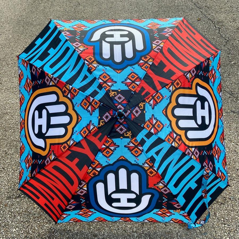 Handeye Supply Co Arc Umbrella in vibrant blue, red, and black with a white hand logo and "HANDEYE" text.