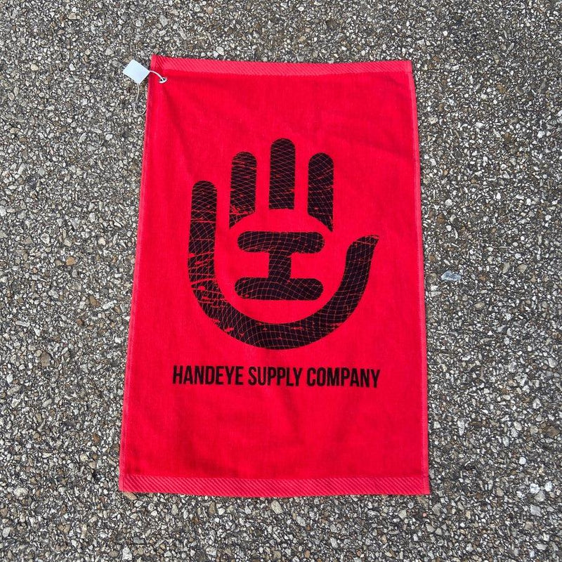 Red cotton Handeye Supply Company disc golf towel with a prominent black hand logo and a white carabiner clip.